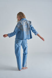 Chaqueta de jean azul claro para mujer de estilo moderno con diseños dorados atras con bolsillos.
