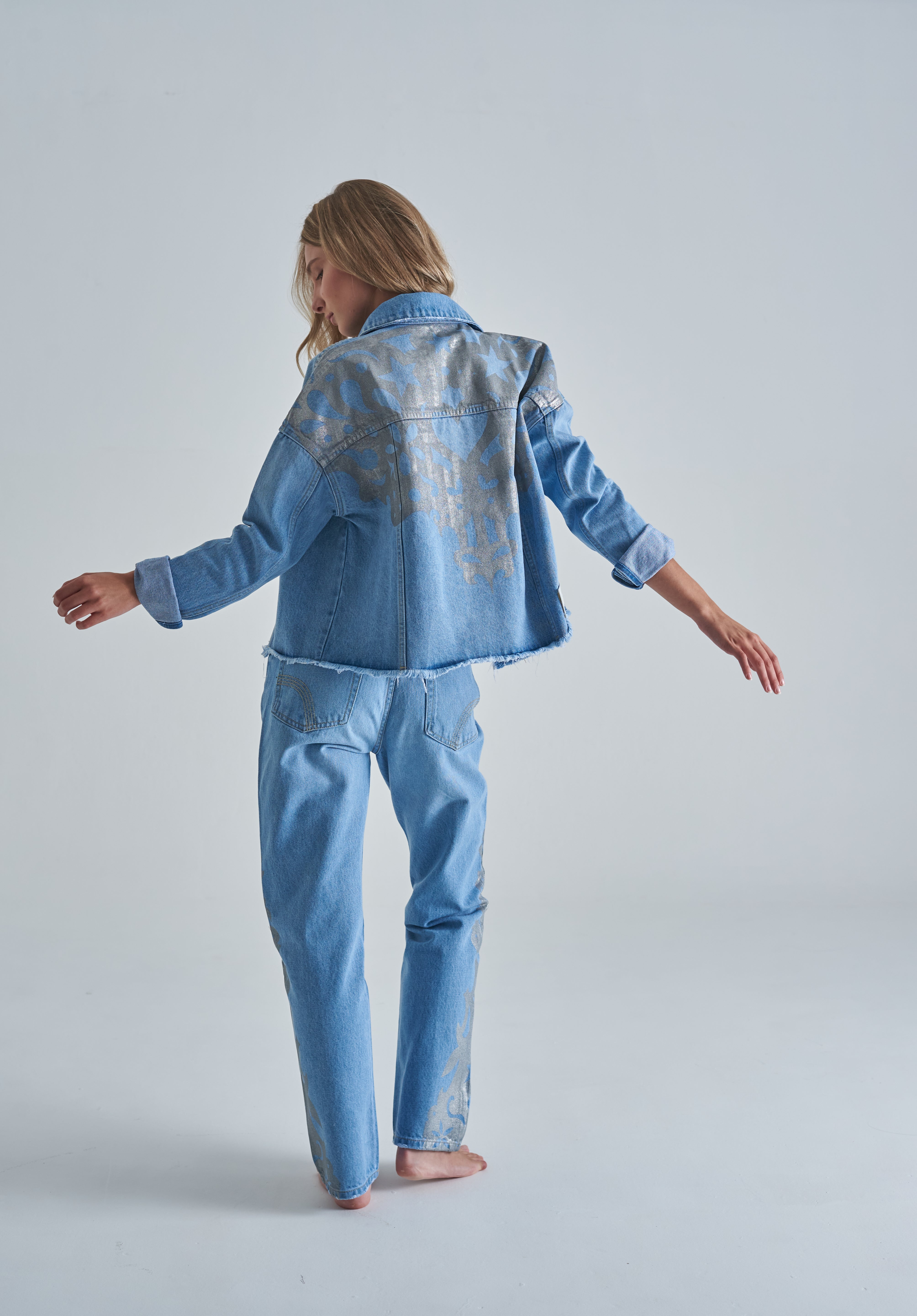 Chaqueta de jean azul claro para mujer de estilo moderno con diseños dorados atras con bolsillos.
